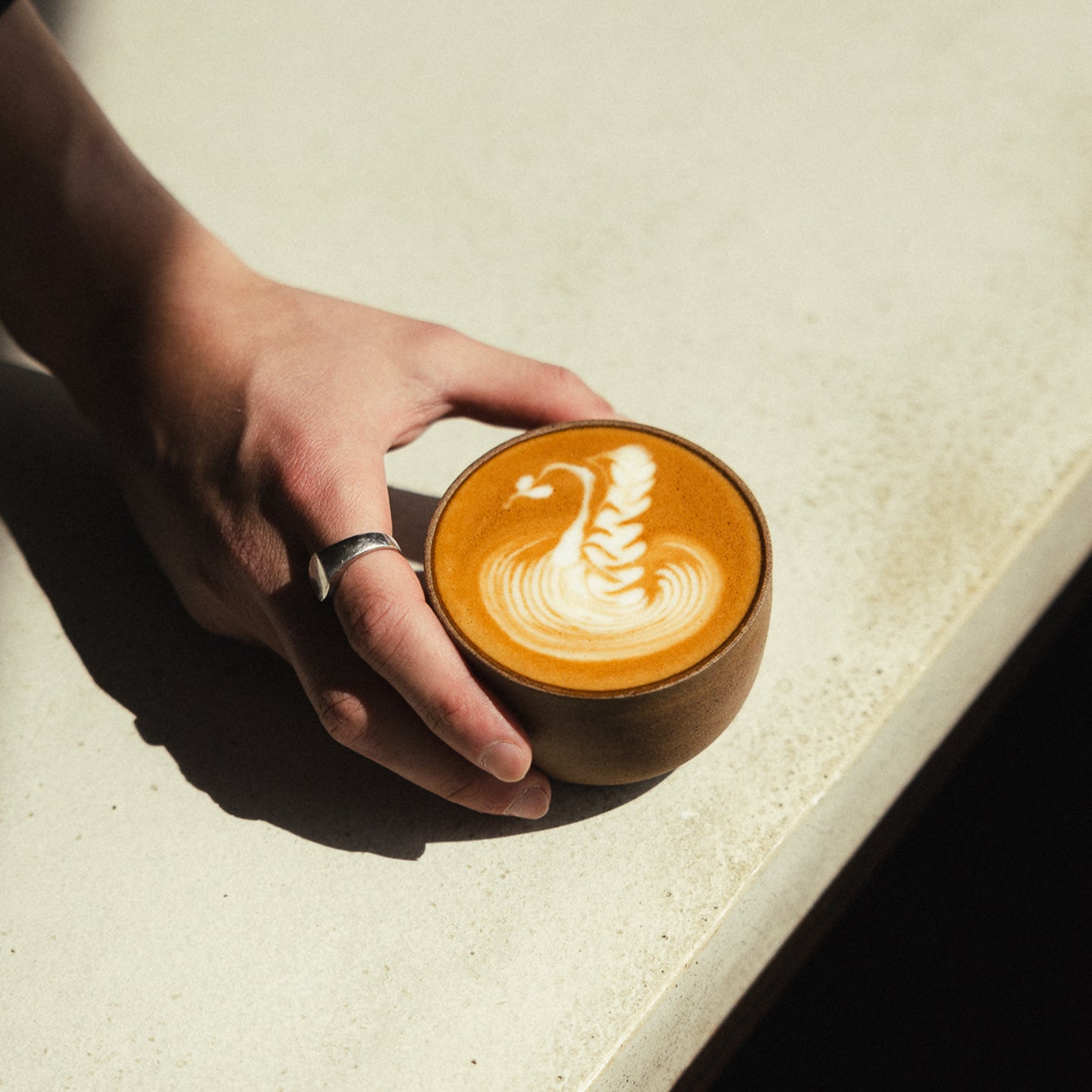 Image of flat white being held by a hand on a coffee shop counter